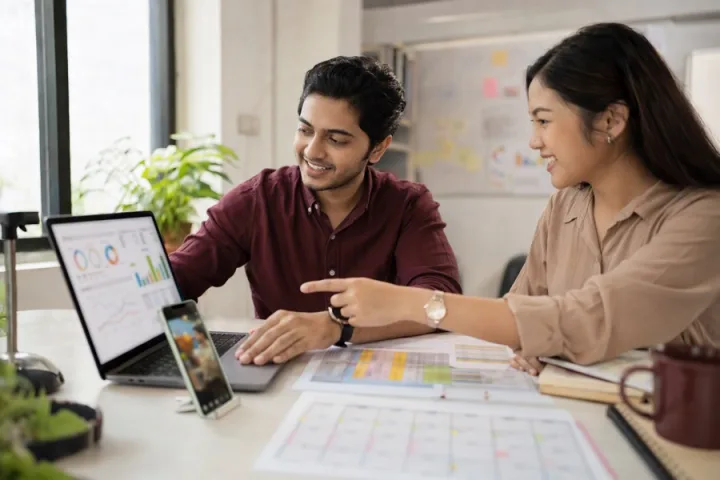 Two young marketers reviewing ad campaign charts on a laptop