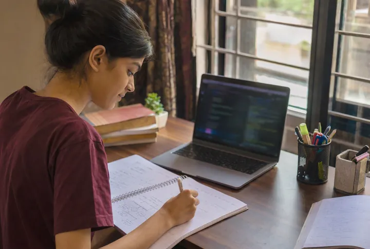 A student studying Python code with a notebook at home